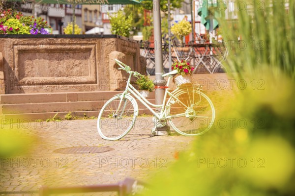 A decorative white bicycle stands in the centre of a lively town square, small town of Perle Calw, Black Forest, Germany