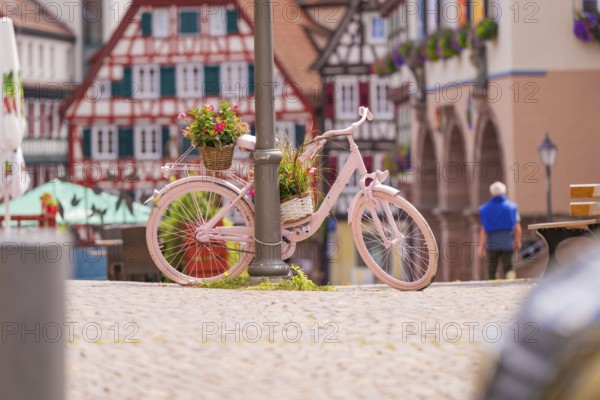Pink bicycle with flowers next to half-timbered houses, an invitation to linger in pleasant weather, small town pearl Calw, Black Forest, Germany