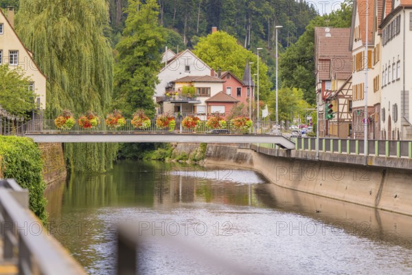 Idyllic scene with flowers on a bridge over a river in a small town surrounded by trees, small town pearl Calw, Black Forest, Germany