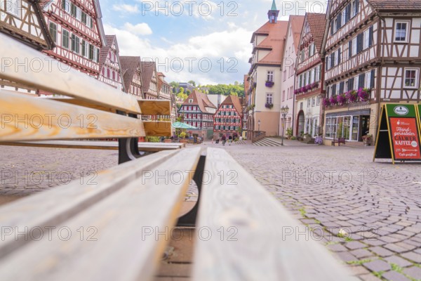 View from a bench onto a market square with half-timbered houses under a blue sky, small town of Perle Calw, Black Forest, Germany