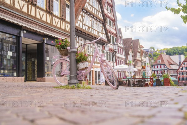 Pink bicycle with a basket of flowers stands on a cobbled street in front of half-timbered houses, small town of Perle Calw, Black Forest, Germany