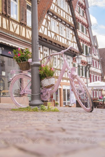 A pink bicycle with a basket of flowers in front of half-timbered houses on a cobbled path, small town of Perle Calw, Black Forest, Germany