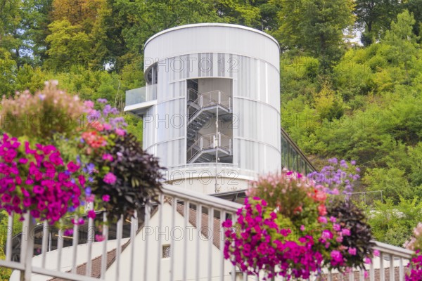 White tower with stairs surrounded by green trees, colourful flowers in the foreground, small town pearl Calw, Black Forest, Germany