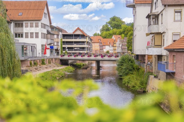 Urban river course with bridge flanked by modern buildings and summer flowers, small town pearl Calw, Black Forest, Germany