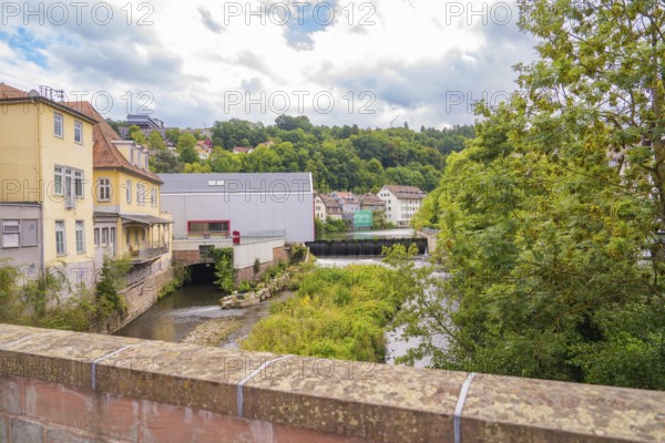River landscape with bridge and surrounding nature under cloudy sky, small town Perle Calw, Black Forest, Germany