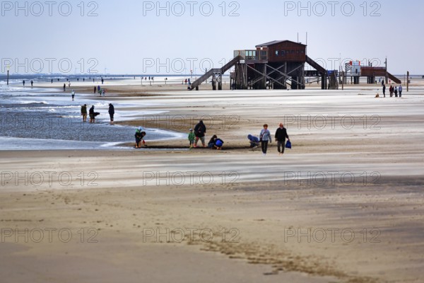 Walkers on the beach, pile dwelling and Westerheversand lighthouse on the horizon, wind, Sankt Peter-Ording, Eiderstedt peninsula, Wadden Sea National Park, North Sea, North Frisia, Schleswig-Holstein, Germany