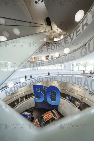 Interior of an exhibition decorated with a curved staircase and large numbers, BMW Welt, Munich, Germany