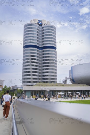 High-rise building next to a modern round building, visited by many people under a partly cloudy sky, BMW Welt, Munich, Germany