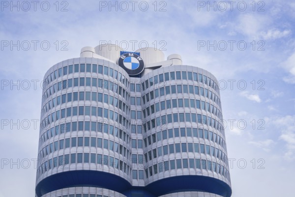 High-rise building with round glass facades and prominent logo against a slightly cloudy sky, BMW Welt, Munich, Germany