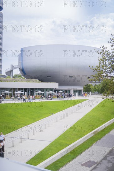 Large modern building surrounded by a green park with people out for a walk, BMW Welt, Munich, Germany