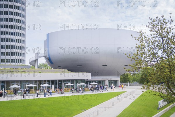 Futuristic-looking building with many visitors and manicured green space in the foreground, BMW Welt, Munich, Germany