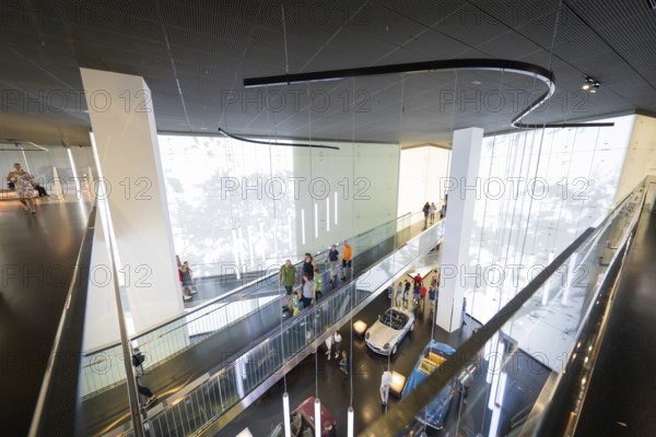 Modern interior with group of visitors and exhibited vehicles under dynamic light installations, BMW Welt, Munich, Germany