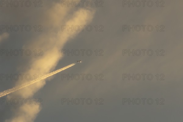Jet passenger aircraft with a vapour trail or contrail flying in a sky with clouds, England, United Kingdom