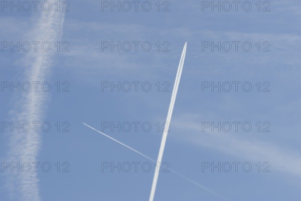 Two jet passenger aircraft with vapour trails or contrails flying in a blue sky crossing making a cross, England, United Kingdom