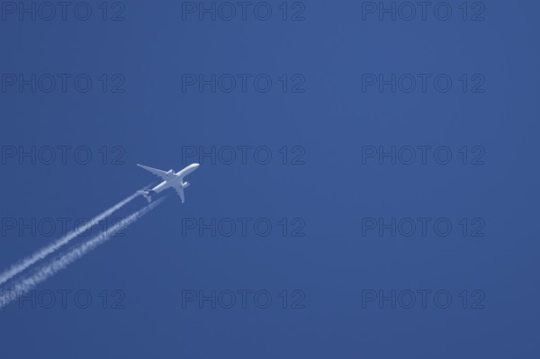 Jet passenger aircraft with vapour trails or contrails behind in a blue sky, England, United Kingdom