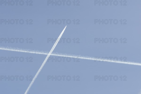 Jet passenger aircraft with a vapour trail or contrail flying crossing another contrail making a cross in the sky, England, United Kingdom