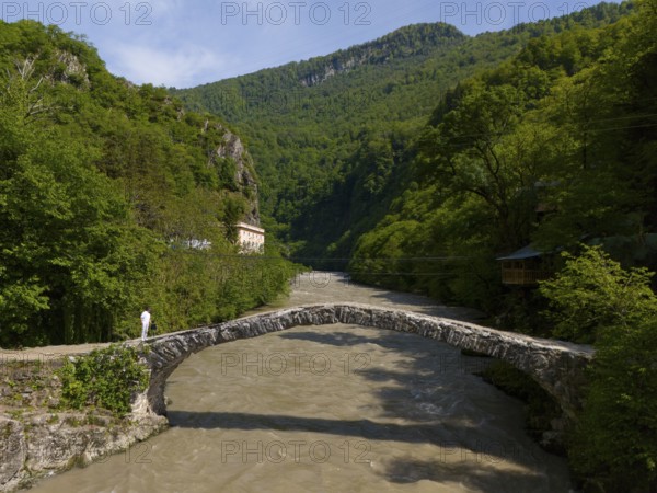 Person crossing a stone bridge over a river, surrounded by green hills and lush forest, aerial view, stone arch bridge Makhuntseti, Adjaristskali River, Adjara Autonomous Republic, Adjara, Adjara, Lesser Caucasus, Georgia