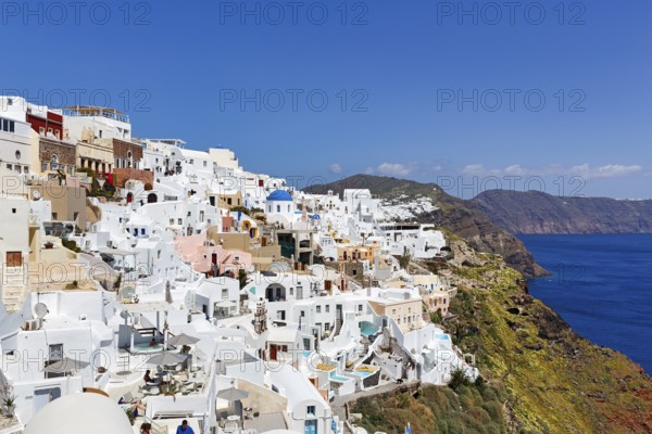 White and colourfully painted holiday homes, orthodox church with blue dome on the edge of the caldera, cliffs, Oia, Thira, Santorini, Cyclades, Greece