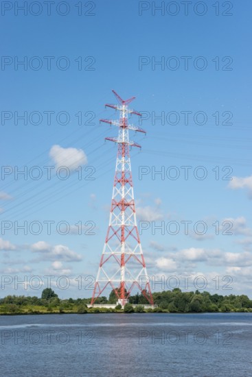 An extremely high electricity electricity electricity pylon, marked white and red, stands on the banks of the Elbe, river bank, Elbe crossing 2, 227 m high, highest overhead line pylon in Europe, surrounded by green landscape with trees and meadows under a blue sky, high-voltage pylon, overhead line pylon, overhead line, colour marking, safety, aviation safety, technology, structure, near Hollern-Twielenfleth, Lühe, Altes Land, Lower Saxony, Germany