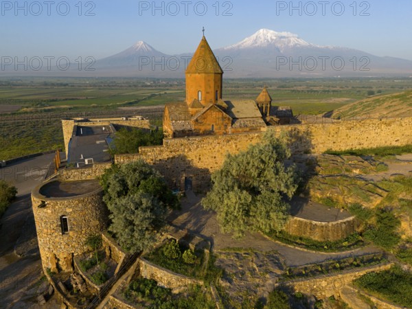 Historic church with stone walls in front of a mountain landscape with blue sky, aerial view, Chor Wirap monastery, Chor Virap, deep dungeon, Ararat and Little Ararat in the background, located in Turkey, Ararat province, Armenia