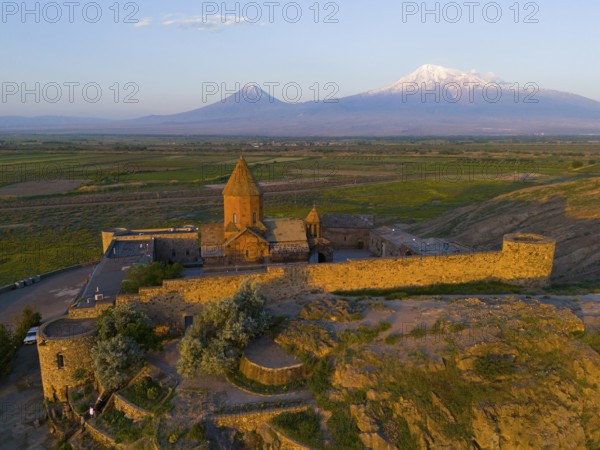 An old church surrounded by walls in front of a mountain range at dawn, aerial view, Chor Wirap monastery, Chor Virap, deep dungeon, Ararat and Little Ararat in the background, located in Turkey, Ararat province, Armenia