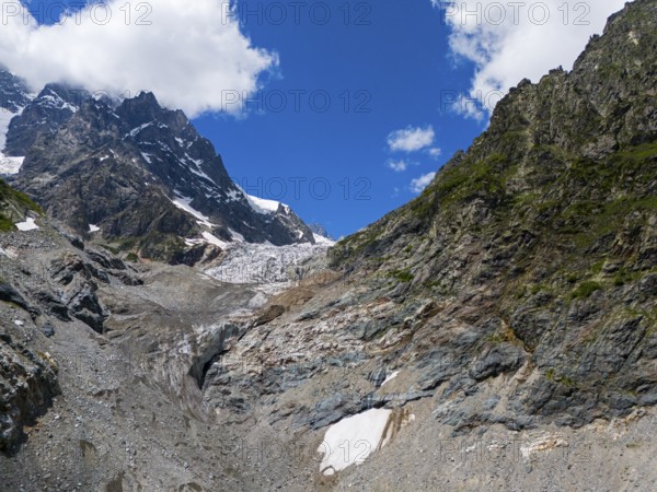 Rocky landscape with a glacier under a blue sky, flanked by mountains. Clouds drift over the alpine valley, aerial view, Chalaadi glacier, Mestia, Svaneti, Caucasus, Georgia