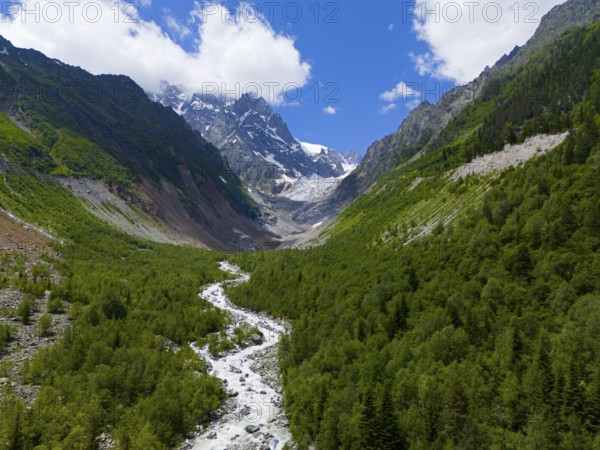 Picturesque mountain landscape with river in the foreground, lush forests and snow-capped peaks under a blue sky, aerial view, Chalaadi glacier, Mestia, Svaneti, Caucasus, Georgia