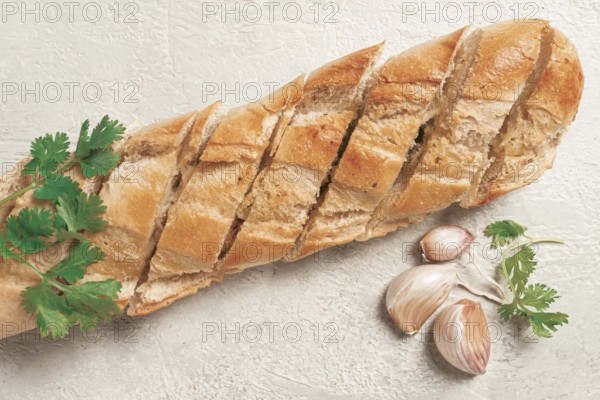 Garlic bread, baguette with garlic butter and herbs, on a light table, top view