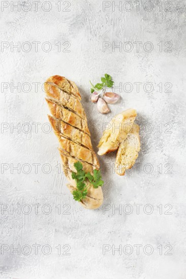 Garlic bread, baguette with garlic butter and herbs, on a light table, top view