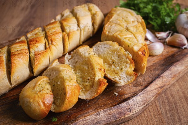 Garlic bread, baguette with garlic butter and herbs, on a wooden board, with herbs and garlic cloves