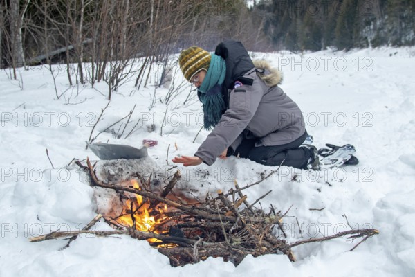 A woman warms herself by a campfire in winter, Gaspesie national park, Province of Quebec, Canada, north America