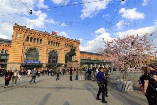 Crowd on station forecourt, Hanover main station in neo-renaissance style, Ernst August Platz with equestrian statue of King Ernst August, cherry blossom, Hanover, Lower Saxony, Germany