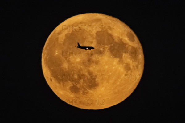 The silhouette of an aeroplane stands out against the full moon, Frankfurt am Main, Hesse, Germany