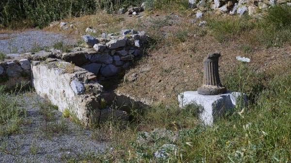 An old wall and a column surrounded by grass and flowers, ancient Roman bath, Tallaras, Analipsi, Maltezana, Astypalea, Astipalea, Astipaleia, Dodecanese, Greek Islands, Greece