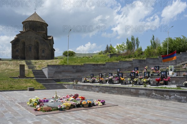 Church with cemetery in the foreground, decorated with flowers and Armenian flag under a cloudy sky, Sisian, Sissian, Sjunik province, historically Sangesur, Armenia