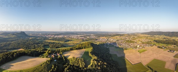 Luftbild, Panorama von einer vulkanisch geprägten Landschaft im Abendlicht, im Vordergrund der Phonolithkegel Rosenegg, am Horizont die Hegauberge mit dem Hohentwiel und der Stadt Singen und der angrenzenden Gemeinde Rielasingen-Worblingen, Hegau, Landkreis Konstanz, Baden-Württemberg, Deutschland