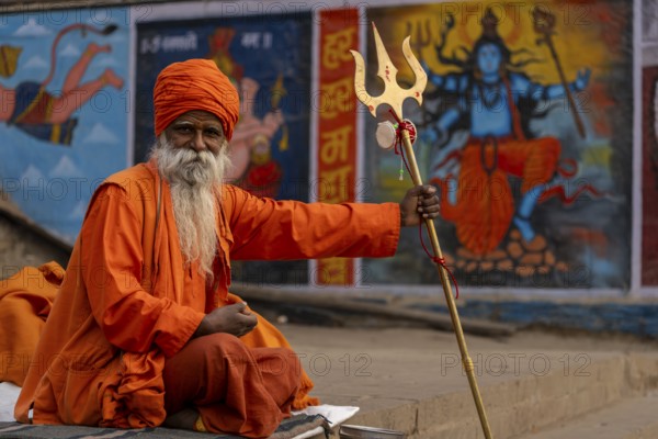 Indian sadhu holding trident, with image of Shiva in the background, Bangali Tola, Varanasi, Uttar Pradesh, India