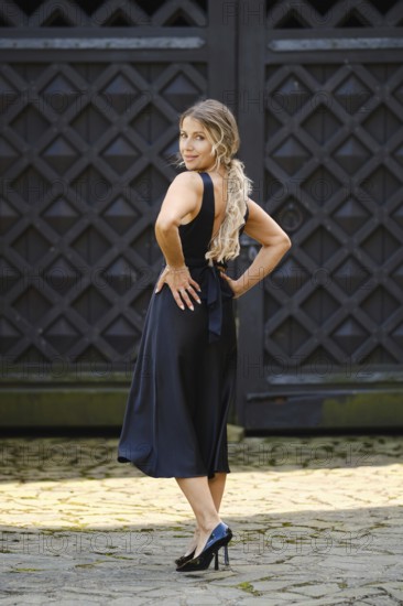 A middle-aged woman stands with her back turned, showcasing her fashionable dress and high heels