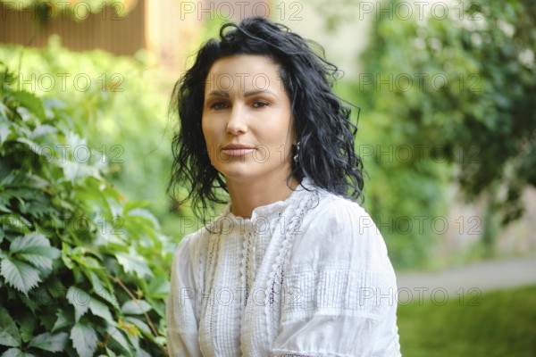 Bright and peaceful atmosphere surrounds a woman with curly black hair as she sits gracefully among vibrant green plants. Her expression is calm and thoughtful, reflecting the tranquility of nature