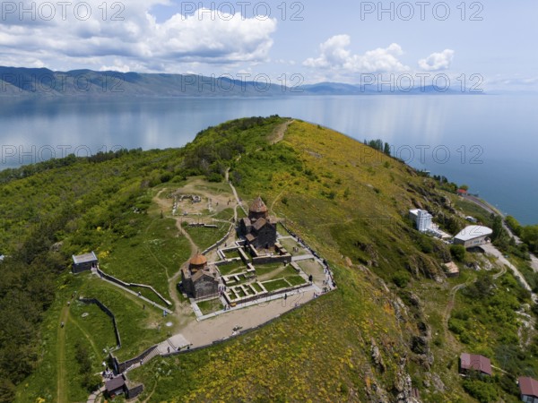 Panorama of a monastery on a green hill with a view of a lake and mountains under a cloudy sky, aerial view, Sevanavank Monastery, Sevan Monastery, Gegharkunik Province, Armenia