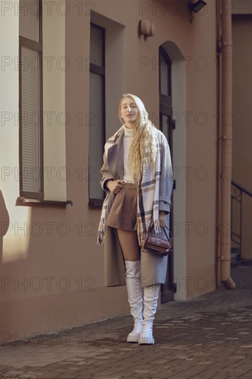 The young woman exudes confidence in a chic autumn outfit featuring a brown skirt and white knee-high boots