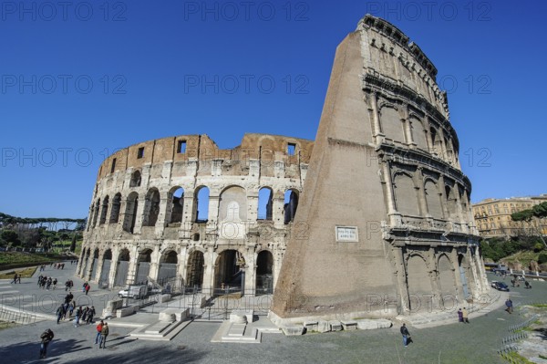 View from east southeast to ancient Colosseum from ancient Rome right partially preserved up to the height of top tiers floors partially restored facade exterior facade, in the centre under papal memorial plaque of Pope Benedict XIV for martyrs so-called gladiator gate access to arena of Colosseum, Rome, Lazio, Italy