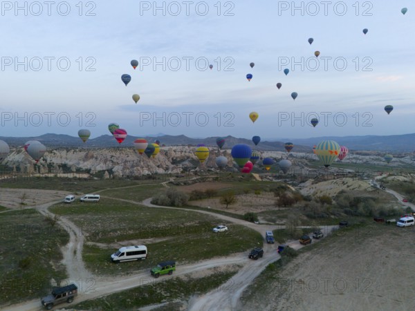Balloons rise into the sky while vehicles stand on the ground in an open landscape, aerial view, Göreme National Park, Göreme Tarihî Millî Parki, Nevsehir Province, Nevsehir, Cappadocia, Cappadocia, Kapadokya, Cappadocia, Central Anatolia, Turkey