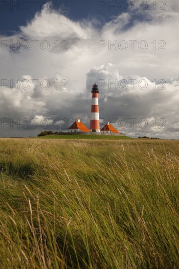 Illuminated Westerheversand lighthouse on the North Sea under dark storm clouds