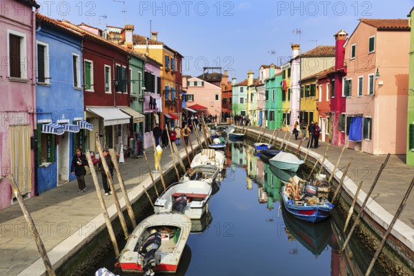 Strollers along the canal, typical street scene in winter, boats, colourful facades, various fishermen's houses in Burano, island in the lagoon of Venice, Italy