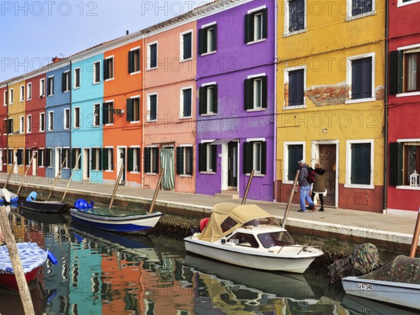 Strollers along the canal, typical street scene in winter, colourful facades, various fishermen's houses in Burano, island in the lagoon of Venice, Italy