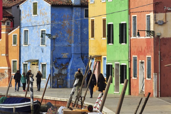 Strollers along the canal, typical street scene in winter, colourful facades in Burano, island in the lagoon of Venice, Italy