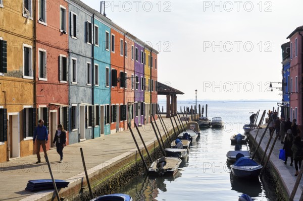 Strollers along the canal, typical street scene in winter, colourful facades of fishermen's houses in Burano, haze, island in the lagoon of Venice, Italy