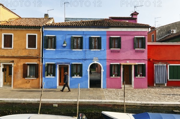 Lone walker on the canal, typical street scene in winter, colourful facades in Burano, island in the lagoon of Venice, Italy