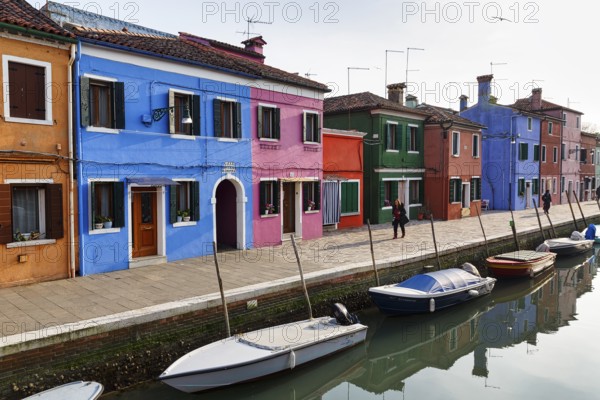 Lone walkers on the canal, typical street scene in winter, colourful facades in Burano, island in the lagoon of Venice, Italy
